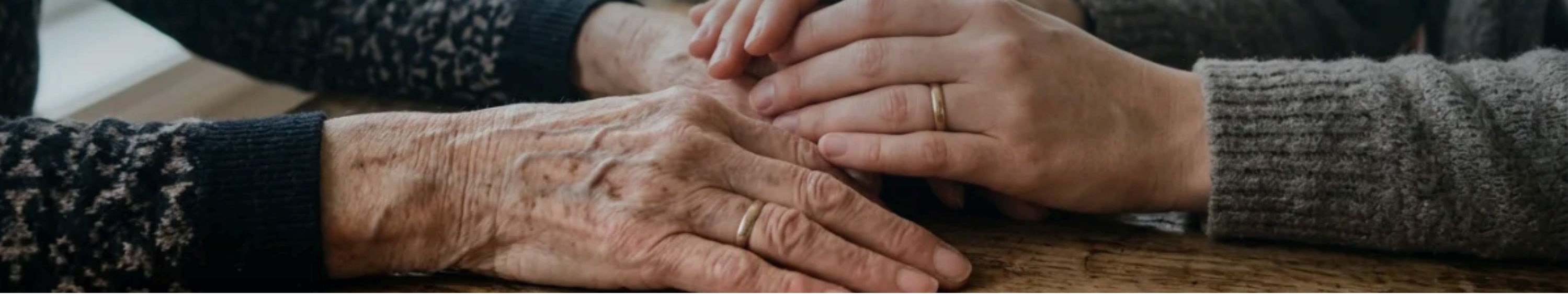 A caregiver holding an older adult’s hands reassuringly across a wooden table